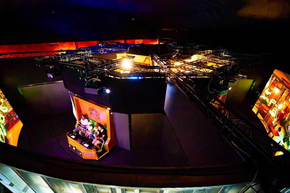 Group on indoor amusement ride surrounded by illuminated screens and overhead rigging.