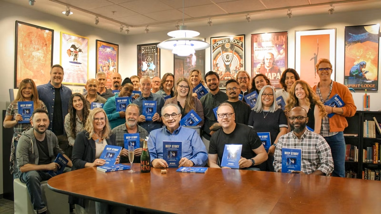 Group photo holding books, gathered around a table in a room with framed posters on walls.