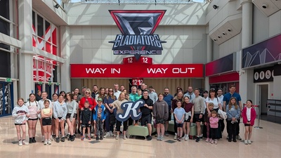 Group photo in front of "Gladiators Experience" entrance sign inside a building.