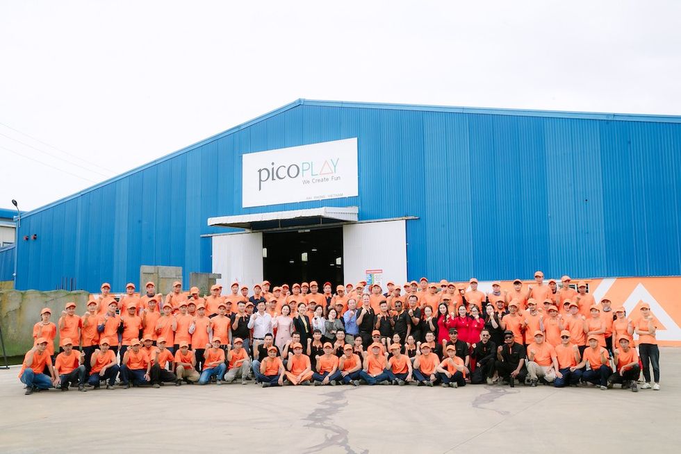 Group photo of employees in orange shirts outside a blue warehouse.