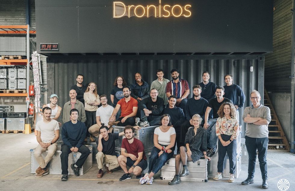 Group photo of people in casual clothing in front of a sign reading "Dronisos".