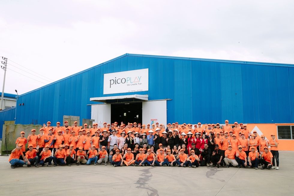 Group photo of Pico Play employees wearing orange shirts in front of a blue building.