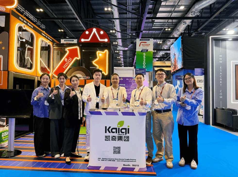 Group posing at a tech expo booth with a colorful backdrop and a "Kaigi Group" sign.