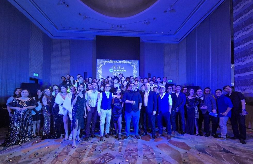 Group posing in formal attire at a Gatsby-themed event with a decorated backdrop.