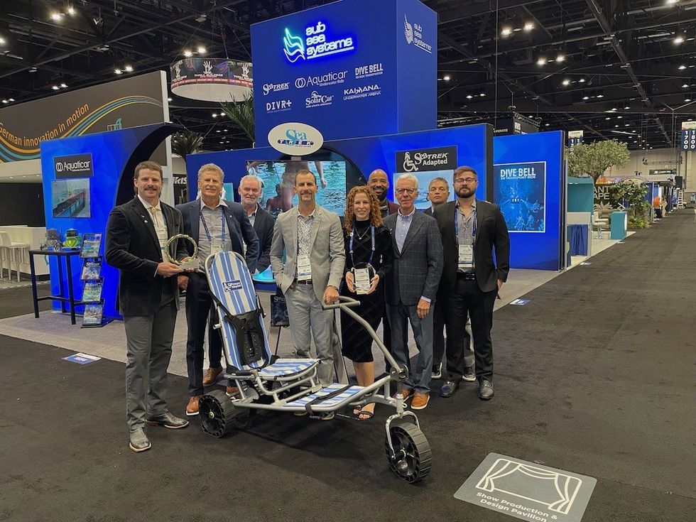 Group posing with an all-terrain wheelchair at a trade show booth.