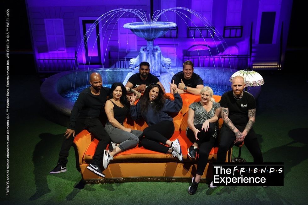 Group sitting on an orange couch in front of a lit fountain at The FRIENDS Experience.