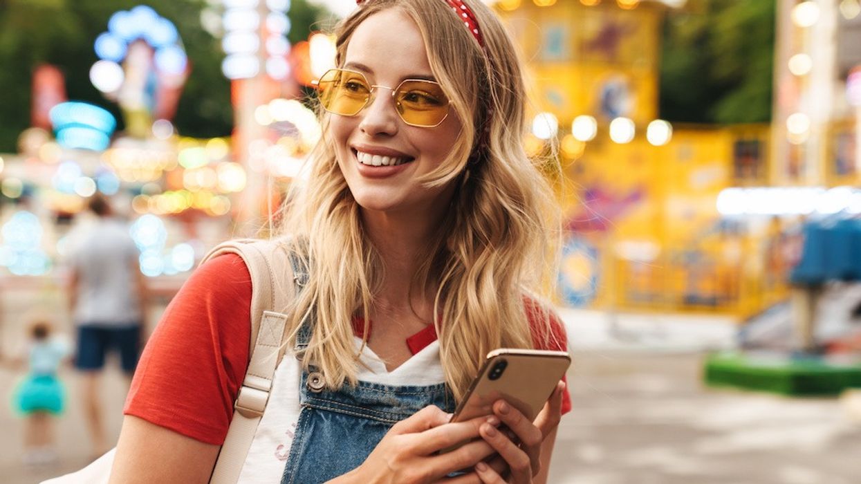 Guest data Image of a smiling young cheery blonde woman in amusement park using mobile phone.
