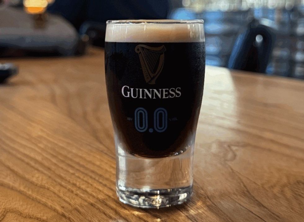 Guinness 0.0 beer on a wooden table in a glass with foam on top.