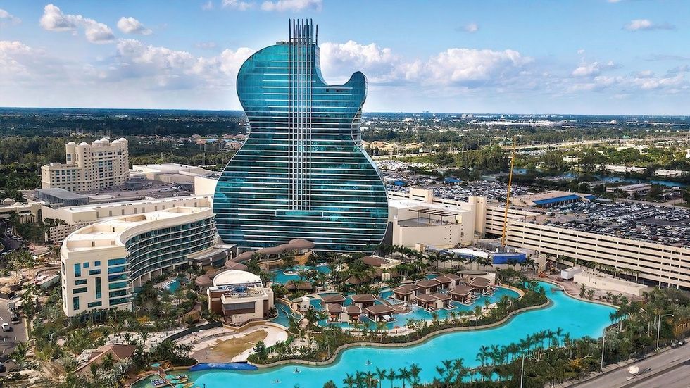 Guitar-shaped building with surrounding resort and pool, set against a blue sky.