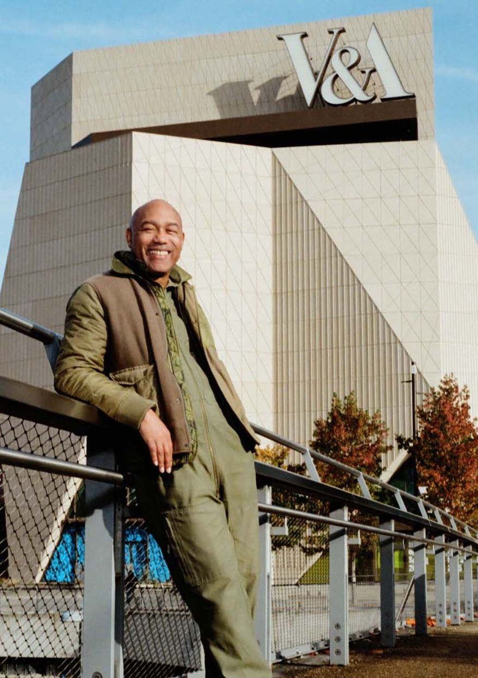 Gus Casely-Hayford in green jacket smiles in front of V&A East Museum building