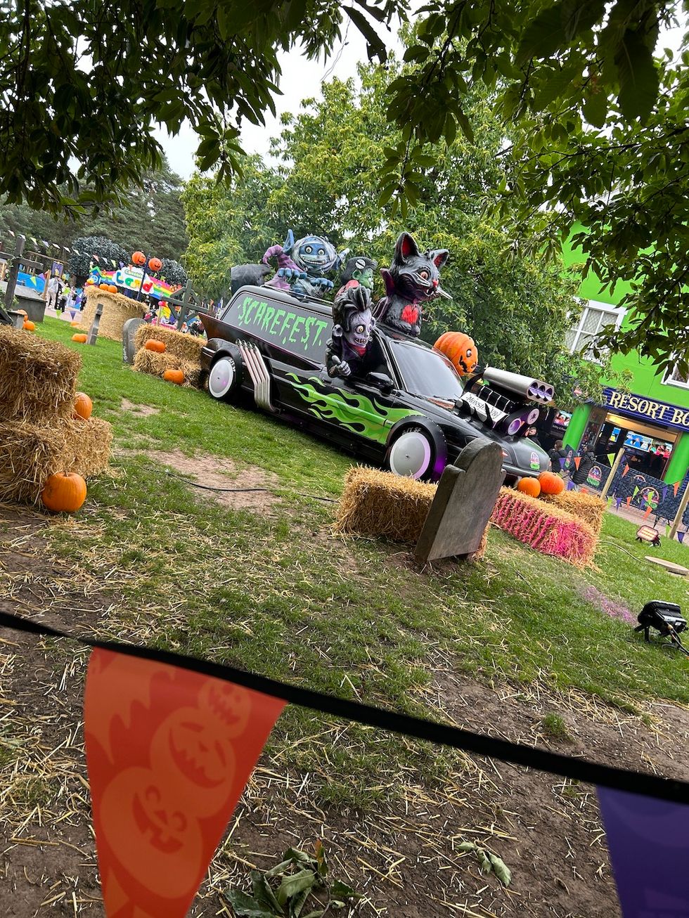 Halloween-themed car with monsters in a park setting, surrounded by pumpkins and hay bales.