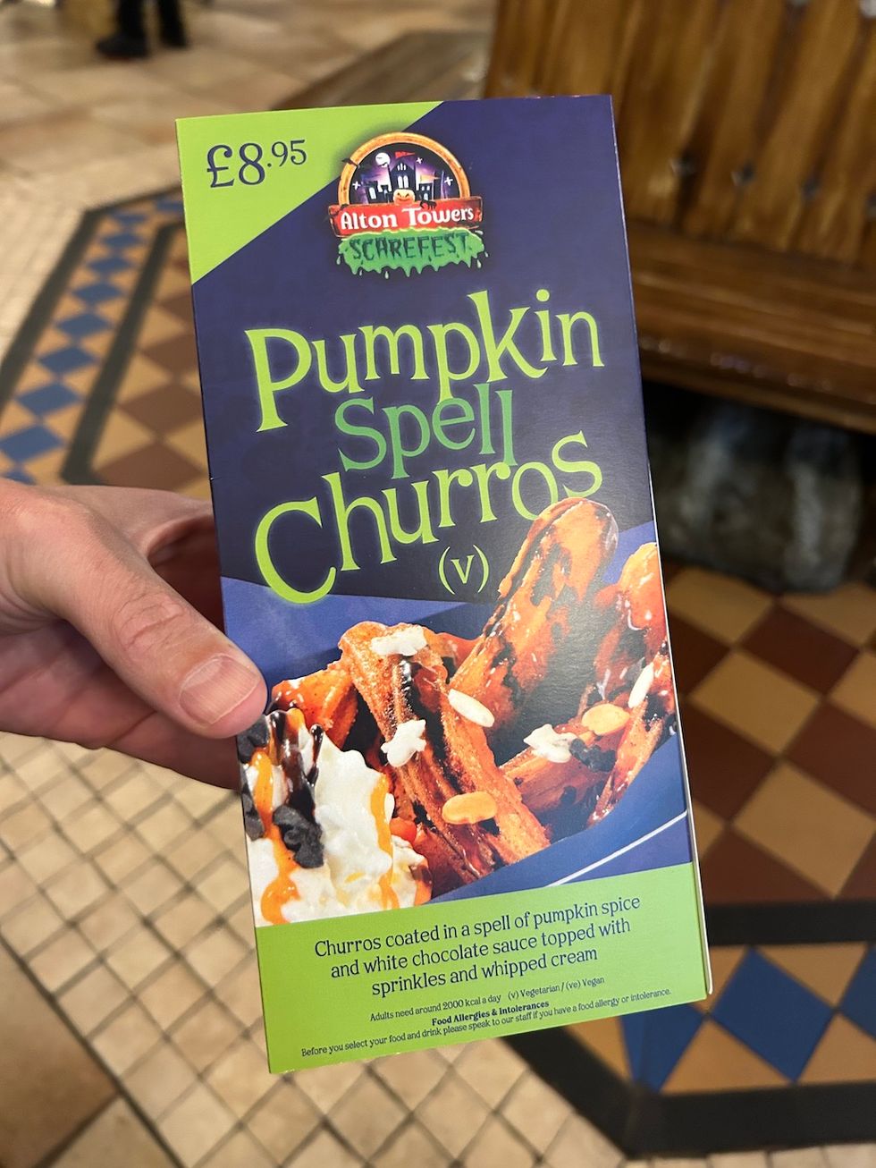 Hand holding a box of "Pumpkin Spell Churros" priced at \u00a38.95 from Alton Towers Scarefest.