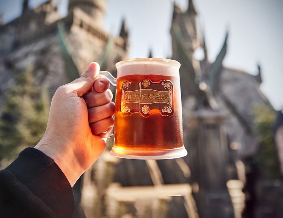 Hand holding a mug of Butterbeer, castle in the blurred background.