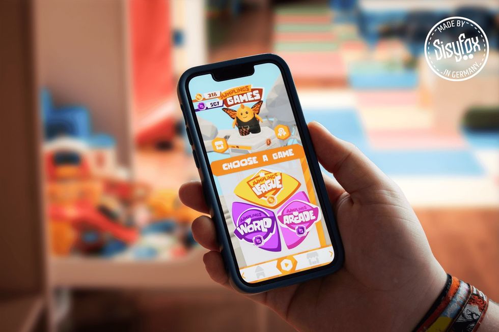 Hand holding a phone showing a game selection screen in a colorful room.