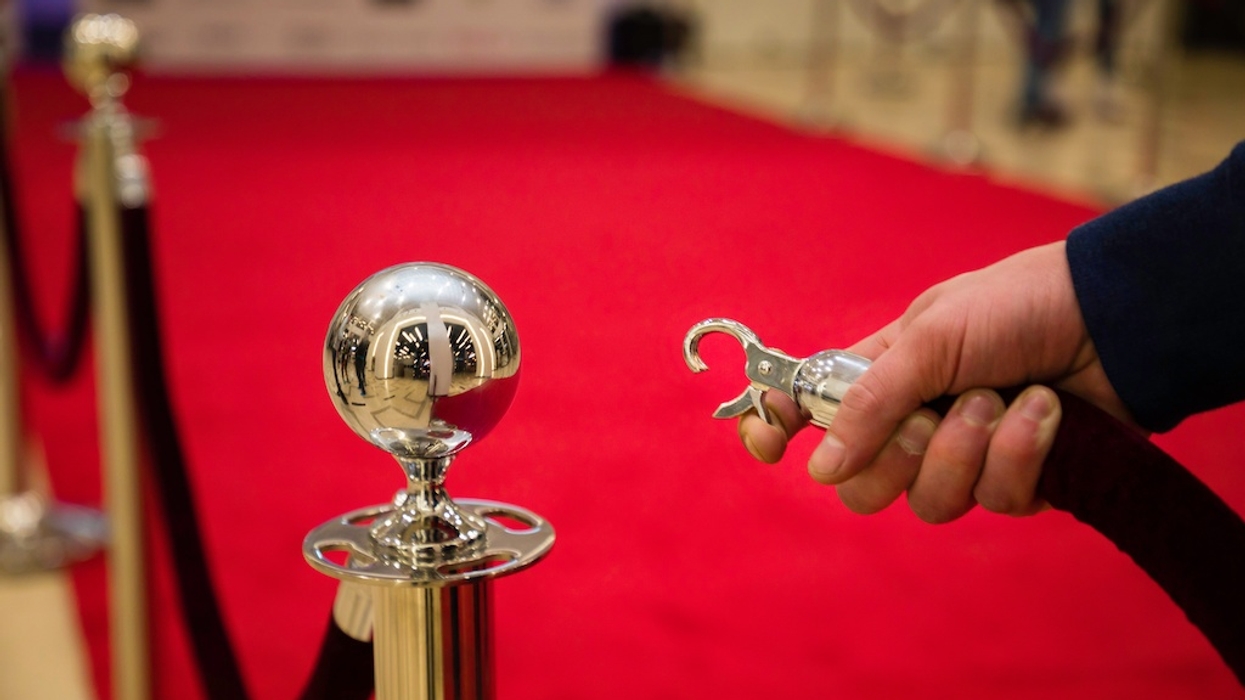 Hand holding a stanchion hook by a red carpet on a polished metal post.
