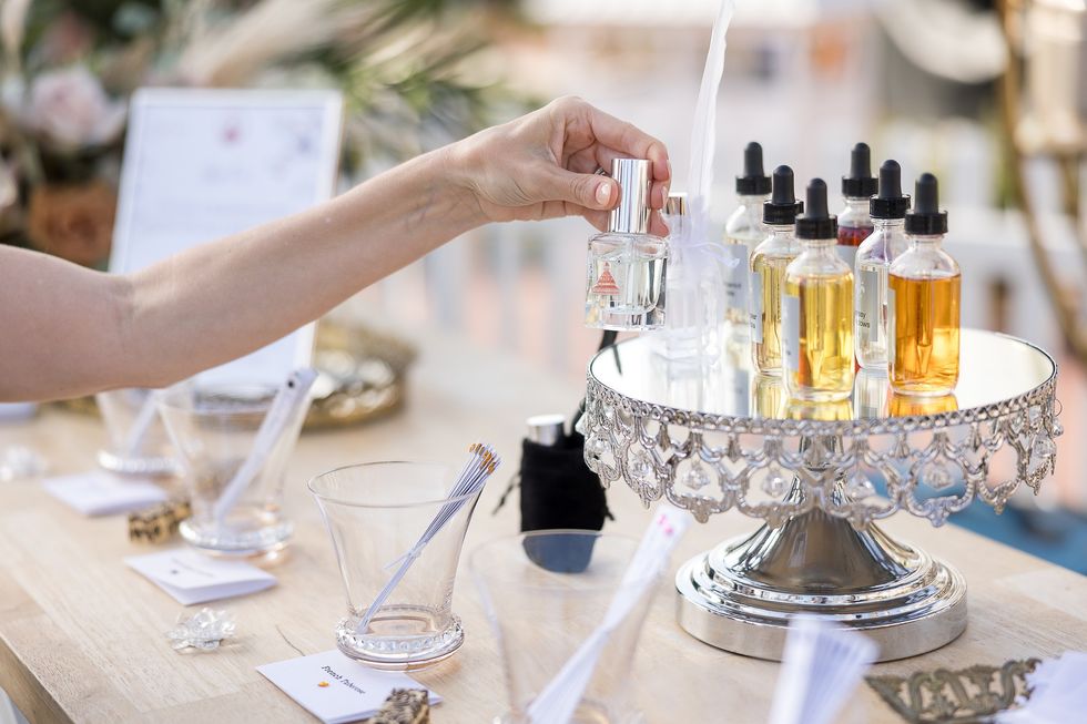 Hand reaching for a perfume bottle on a decorative tray with various oils.