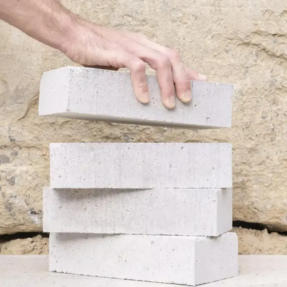 Hand stacking white concrete bricks against a textured wall.