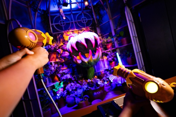 Hands aiming toy guns at a glowing, giant plant in a neon-lit room.