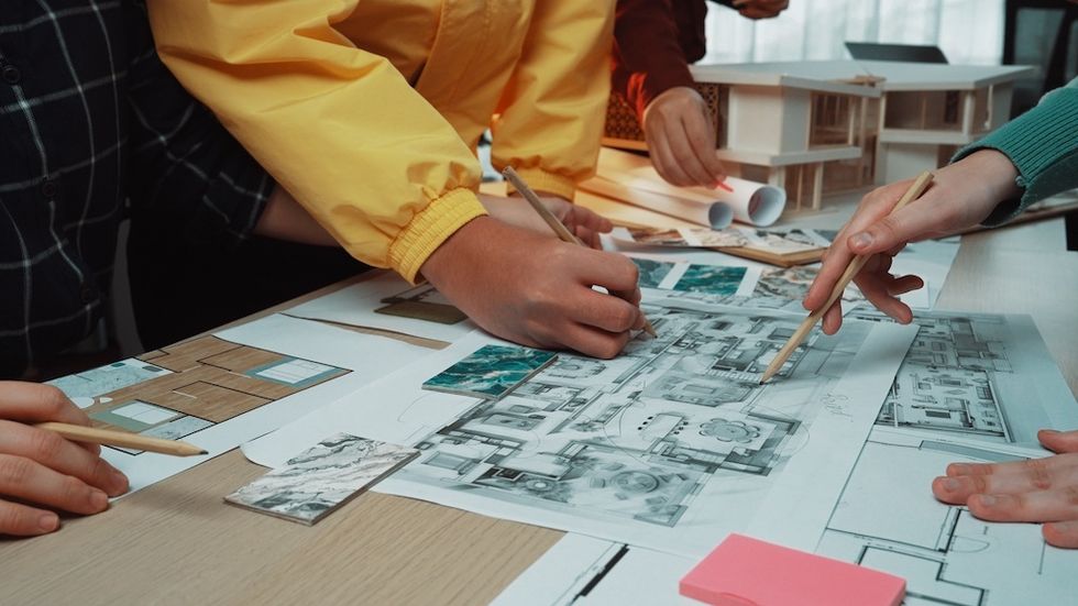Hands collaborate on architectural blueprints and models on a table.