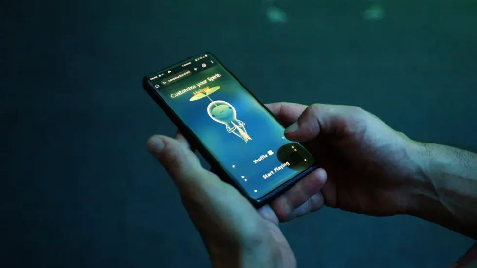 Hands holding a phone displaying a game with a cartoon spirit character.