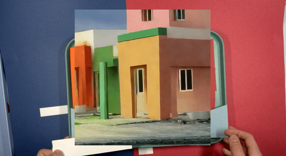 Hands holding a photo of colorful buildings against a red and blue background.