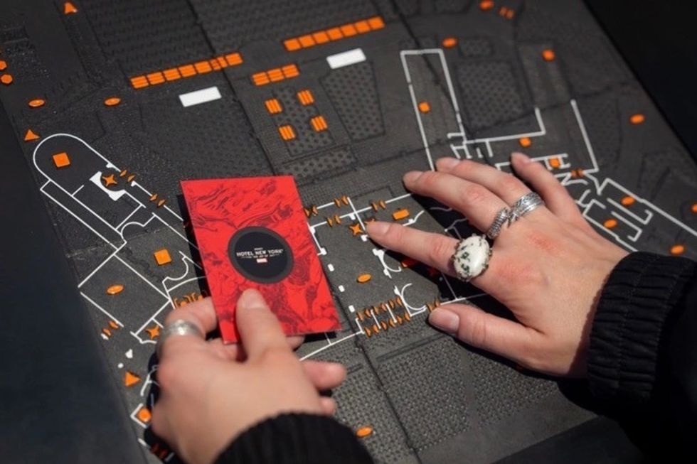 Hands holding a red card over a black tactile map with orange details.