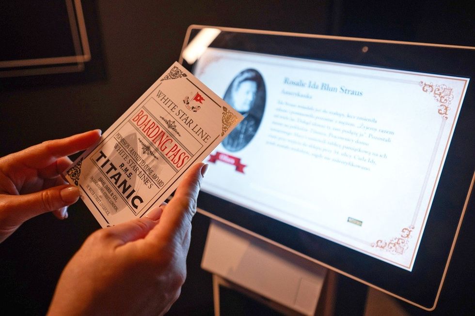 Hands holding a Titanic boarding pass near a touchscreen display.