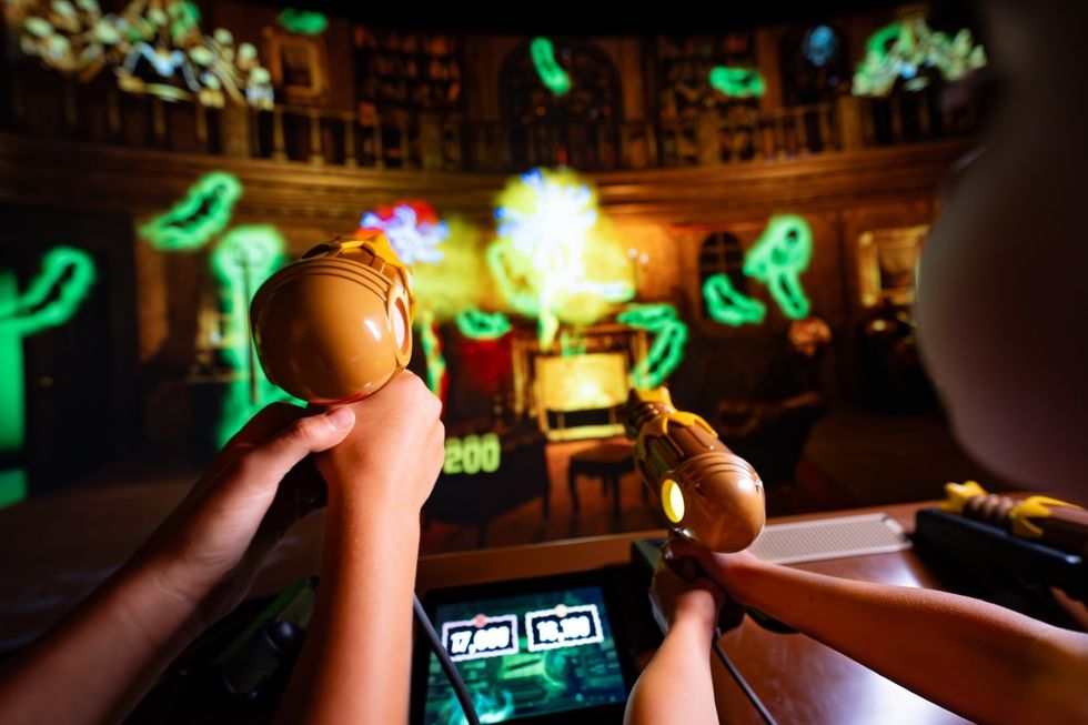 Hands using toy guns in an interactive arcade shooting game with neon targets.