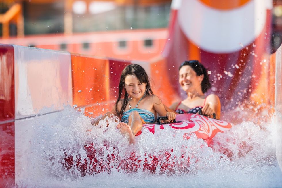 Happy family is quickly sliding on an inflatable circle along the chute from slide. Selective focus on water splash. new water park 2023
