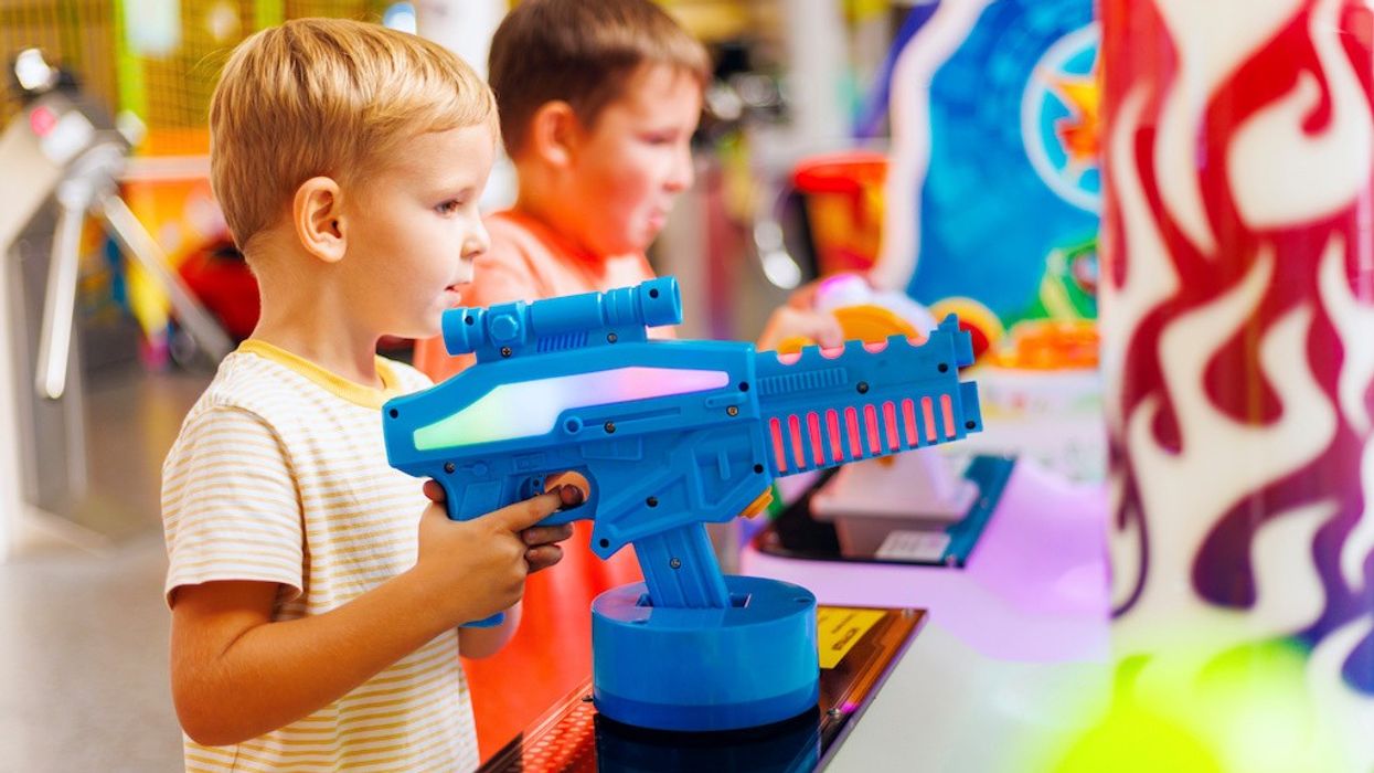 Happy kids playing a shooting game on slot machines at an amusement park.