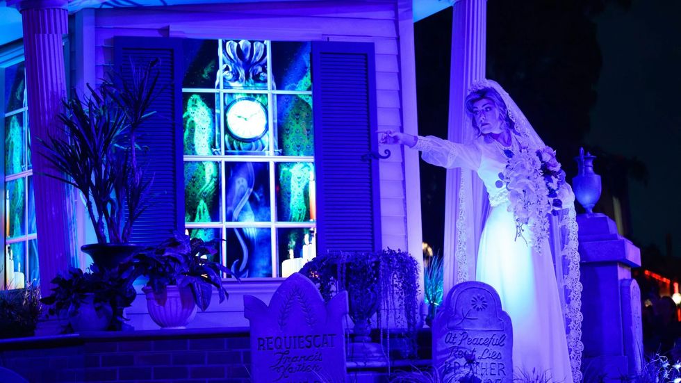Haunted scene at Disneyland's Haunted Mansion with glowing bride, tombstones, and eerie blue lighting.