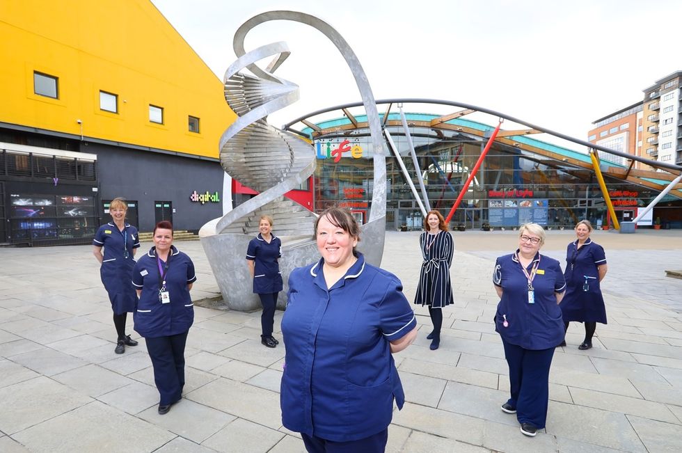 Healthcare workers in uniform at the International Centre for Life, near a spiral sculpture in a plaza.