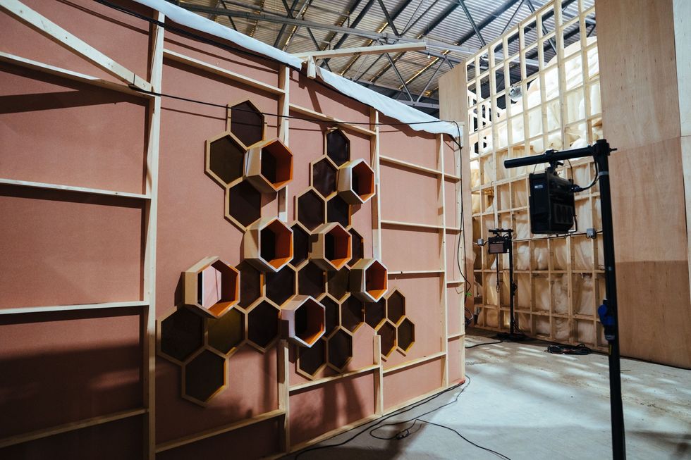 Hexagonal shelves on a studio set wall with lighting equipment nearby.