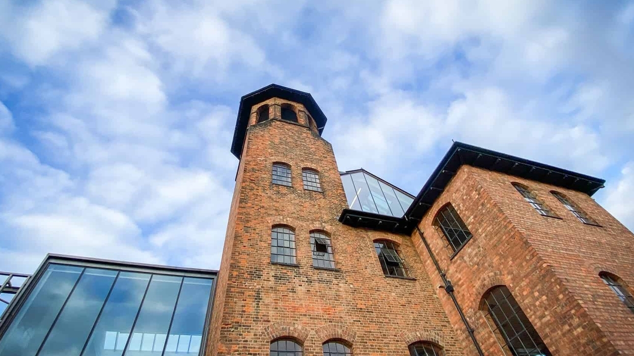Historic brick building with a tall tower against a cloudy blue sky.