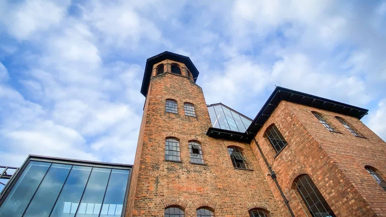 Historic brick building with a tall tower against a cloudy blue sky.