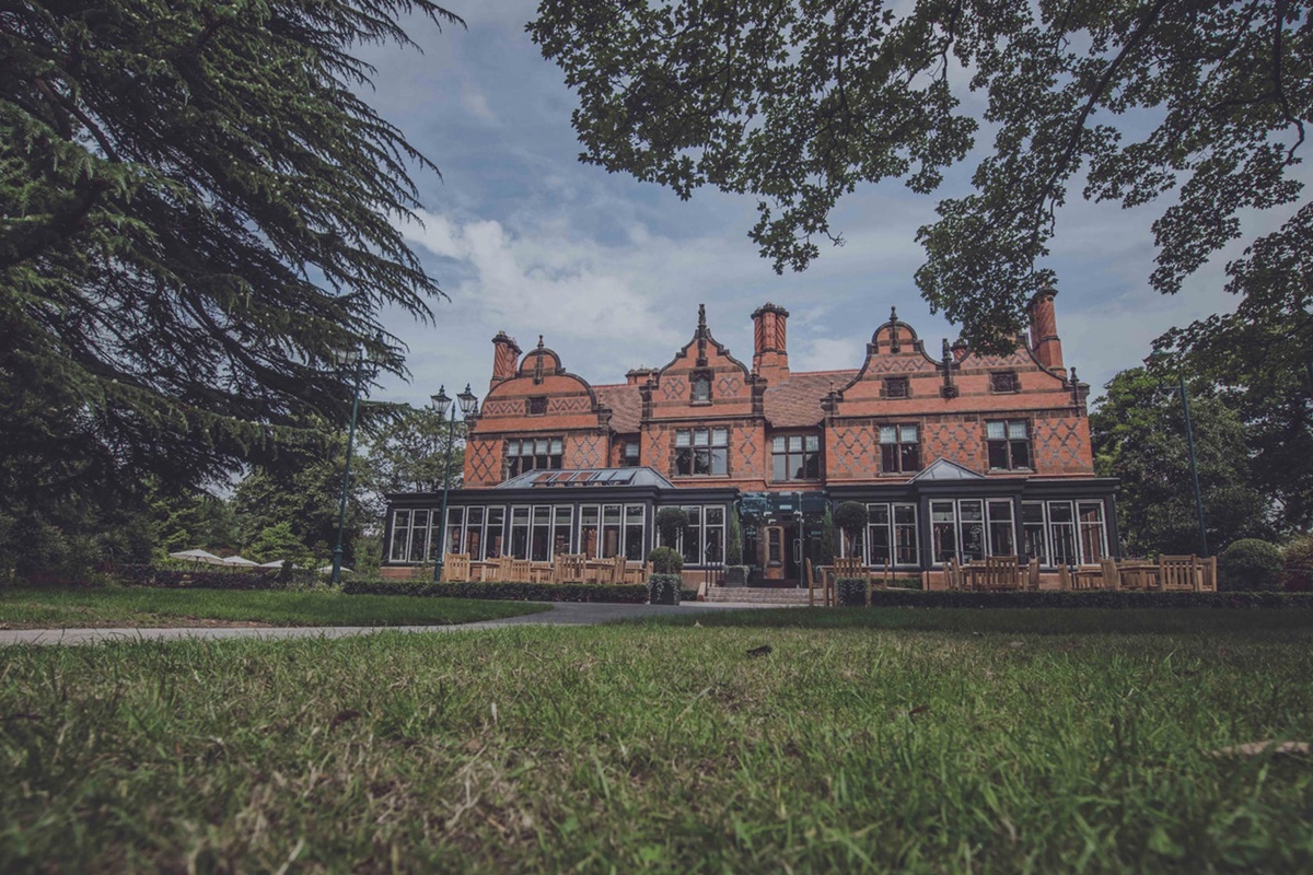 Historic brick manor with ornate roof, surrounded by trees and lawn at Chester Zoo