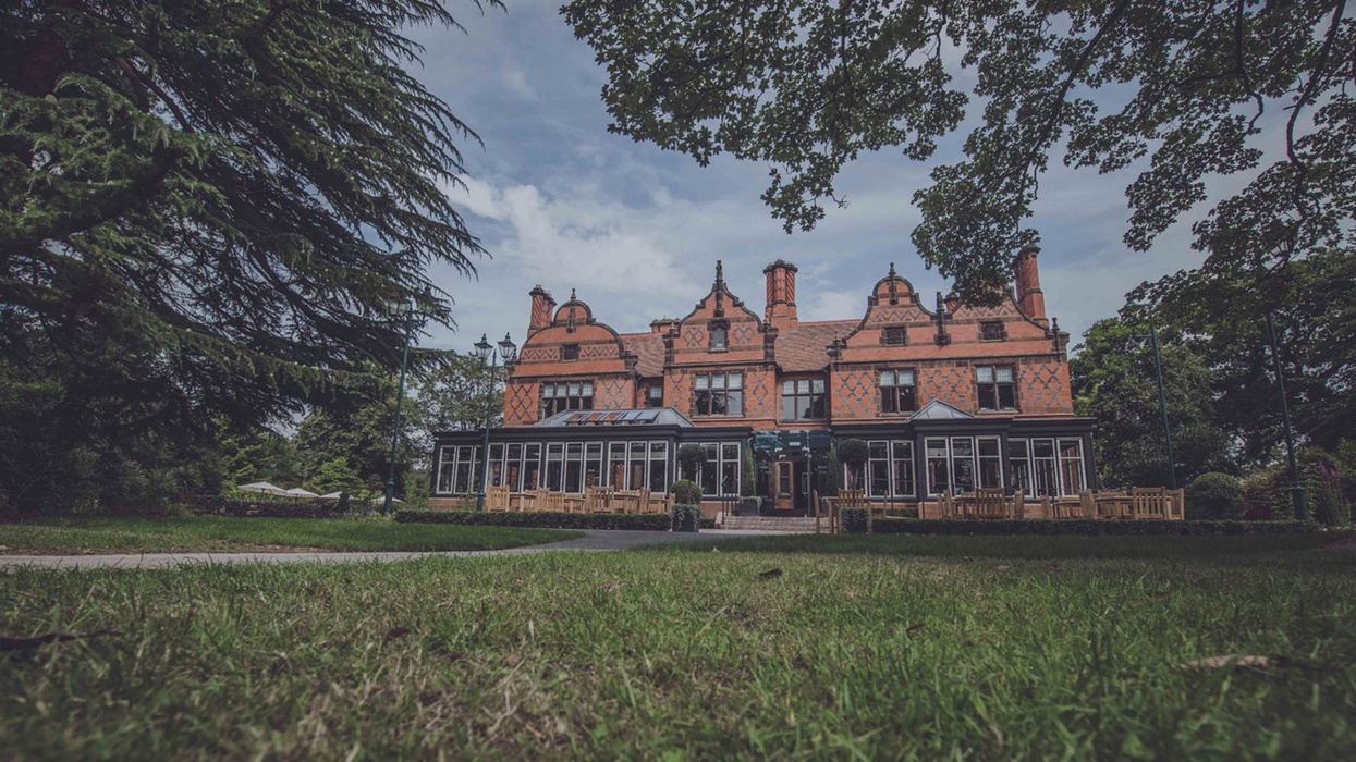 Historic brick manor with ornate roof, surrounded by trees and lawn at Chester Zoo