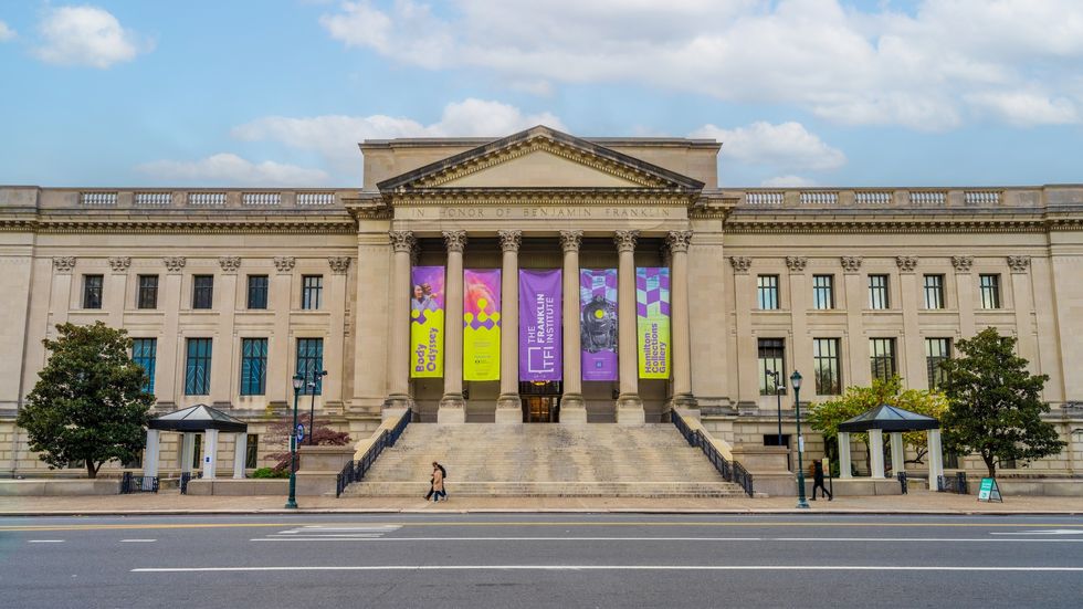 Historic building called the Franklin Institute with columns and colorful banners, viewed from across the street.
