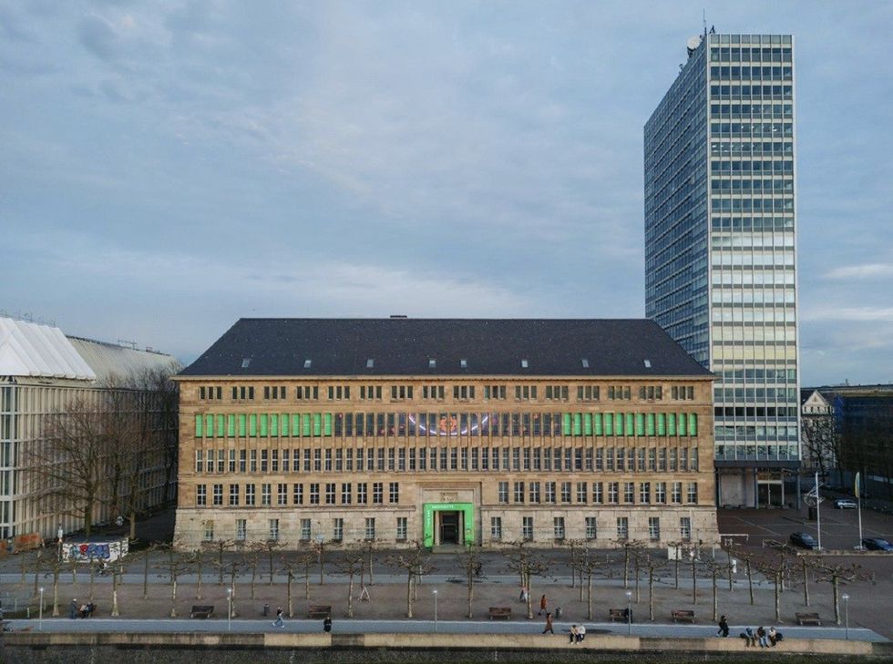 Historic building with green-lit windows, next to a modern high-rise under a cloudy sky.