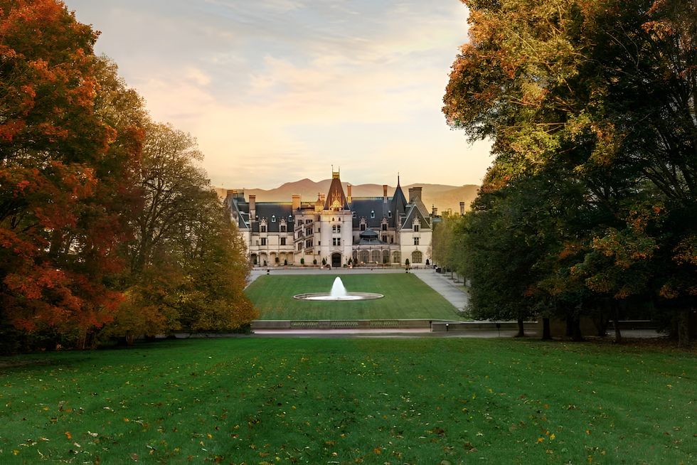 Historic mansion with a fountain, framed by autumn trees under a pastel sky.