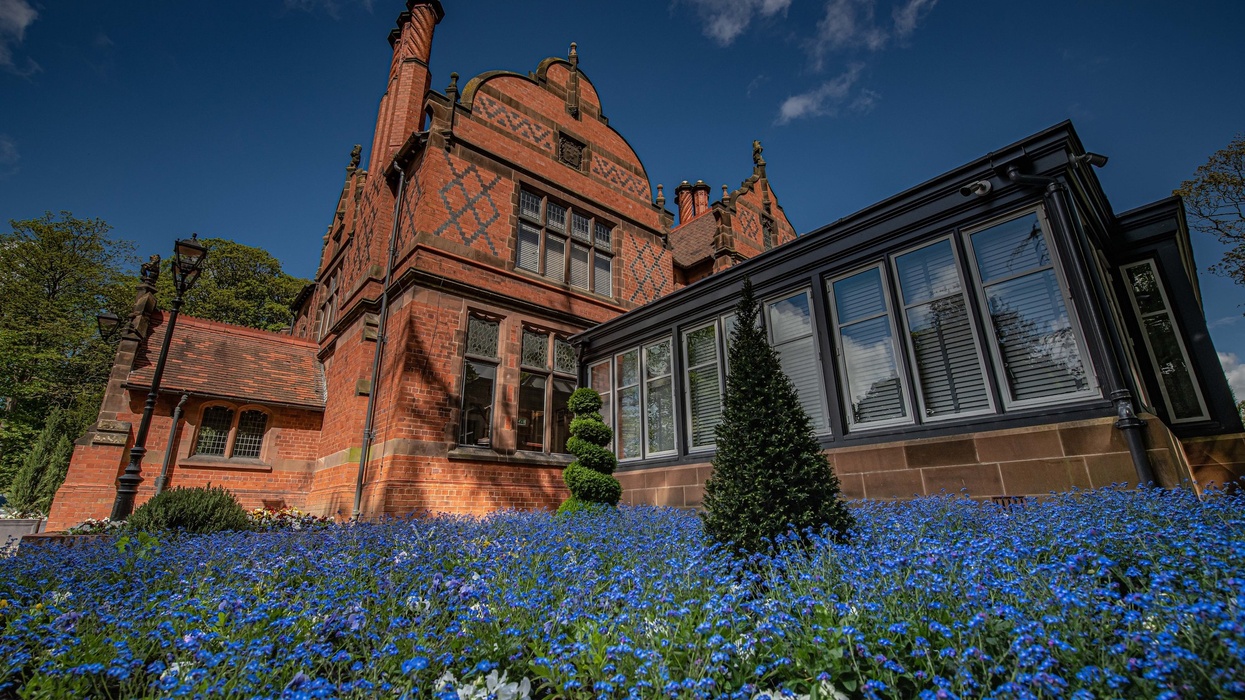 Historic red-brick building at Chester Zoo with ornate facade, surrounded by vibrant blue flowers.