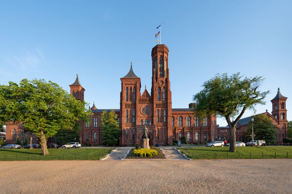 Historic red-brick Smithsonian Castle with lush greenery under a clear blue sky.