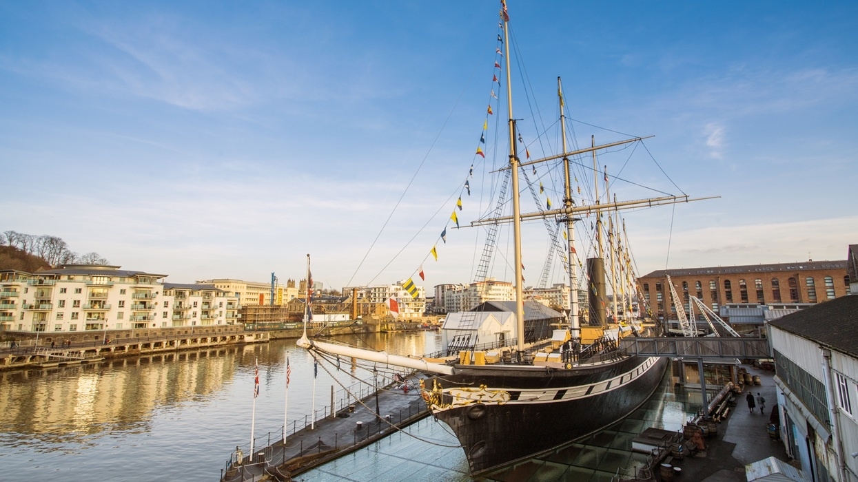 Historic sailing ship at Bristol Dockyards, by waterfront buildings under a clear blue sky.