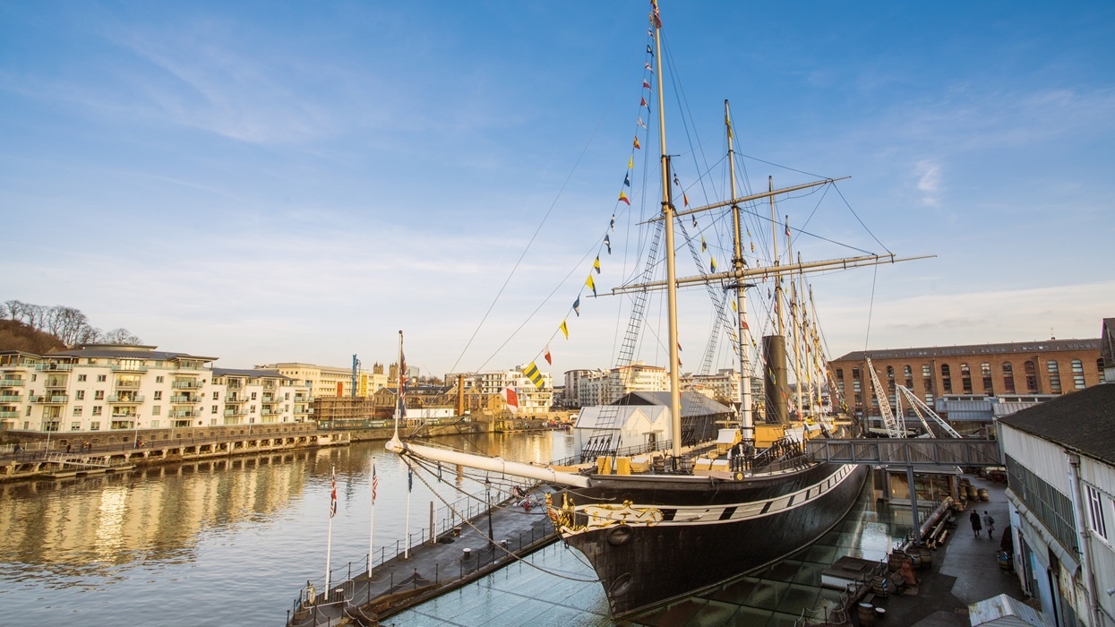 Historic sailing ship at Bristol Dockyards, by waterfront buildings under a clear blue sky.
