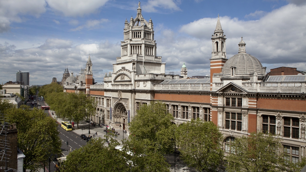 Historic V&A museum building with ornate towers and lush green trees under a partly cloudy sky