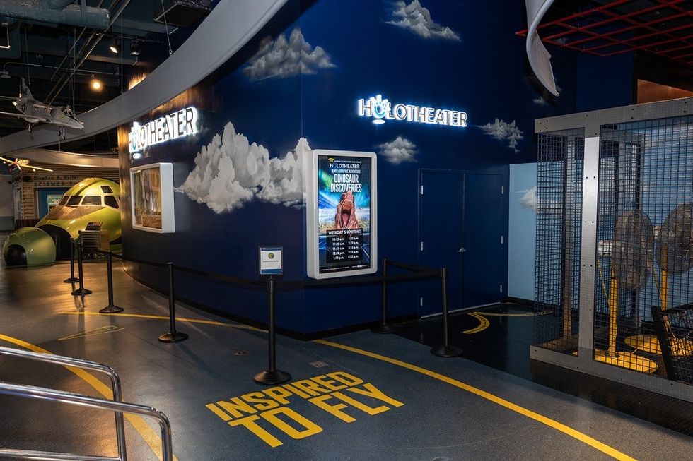 HoloTheater entrance with clouds, airplane decor, and "Inspired to Fly" on the floor.