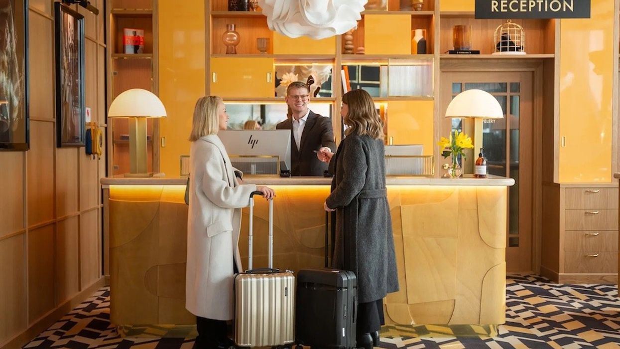 Hotel reception area with two women checking in, man at desk, suitcases in foreground.