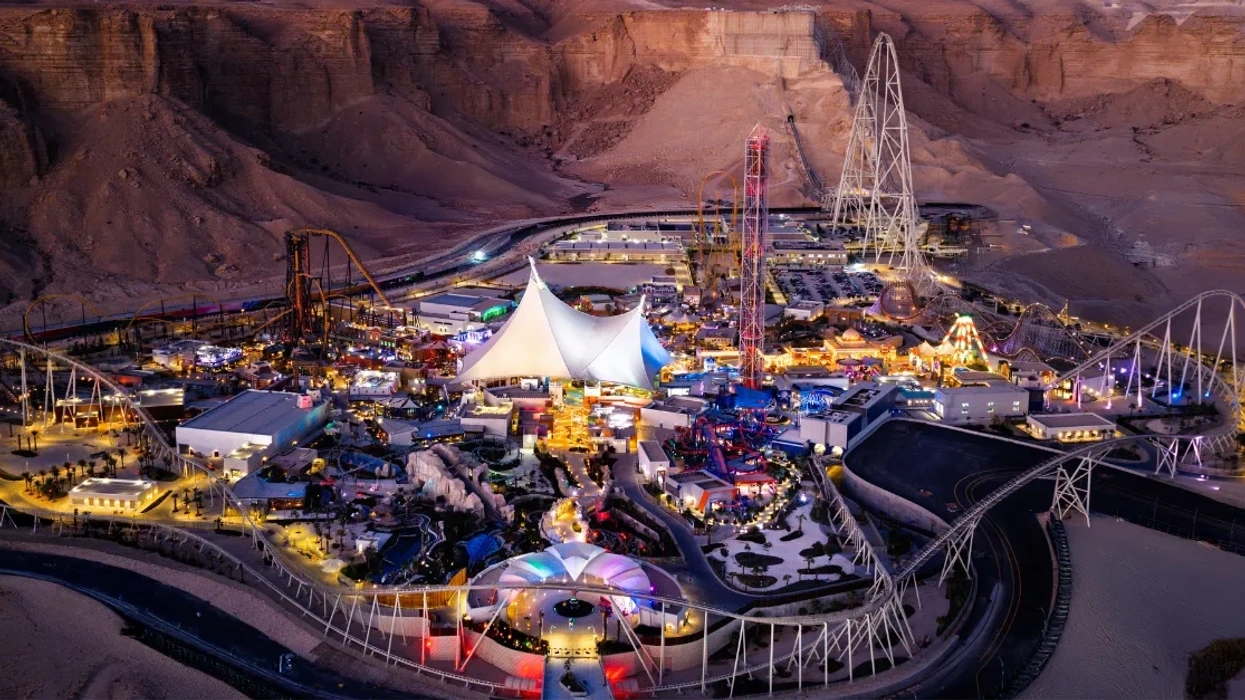 Illuminated amusement park at night, surrounded by desert landscape.