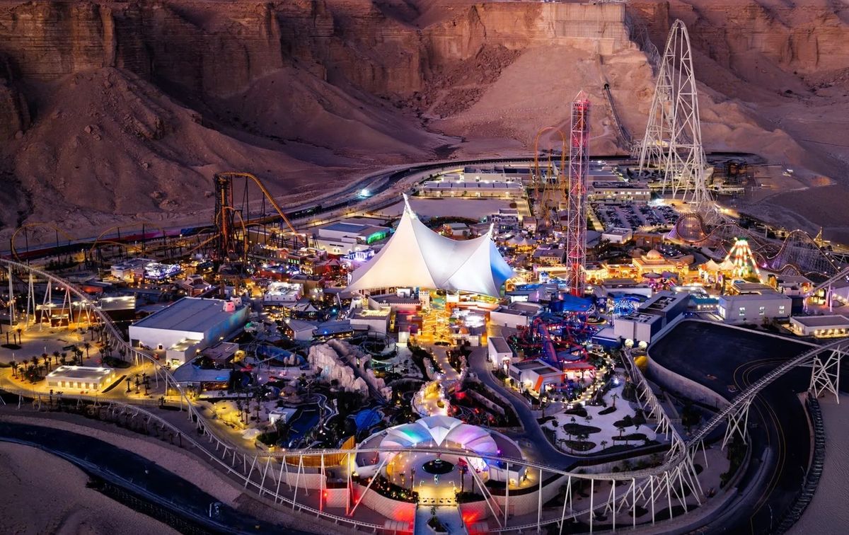 Illuminated amusement park called Six Flags Qiddiya City at night, surrounded by desert mountains.