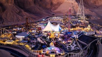 Illuminated amusement park called Six Flags Qiddiya City at night, surrounded by desert mountains.